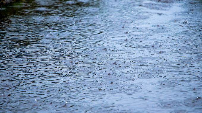 Regen prasselt auf einen Steinboden. Der boden ist mit Wasser bedeckt.