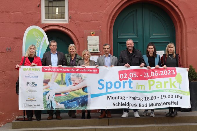 Akteure und Sponsoren stehen vor dem Rathaus hinter einem großen Banner mit dem Schriftzug "Sport im Park"