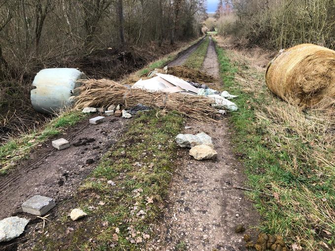 Auf einem Waldweg liegen ein Strohballen, ein Siloballen und weiterer Müll.