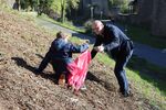 An einem Hang sucht Bürgermeister Sebastian Glatzel ein Beet nach Müll ab und steckt den Fund in die rote Mülltüte eine Schulkindes.