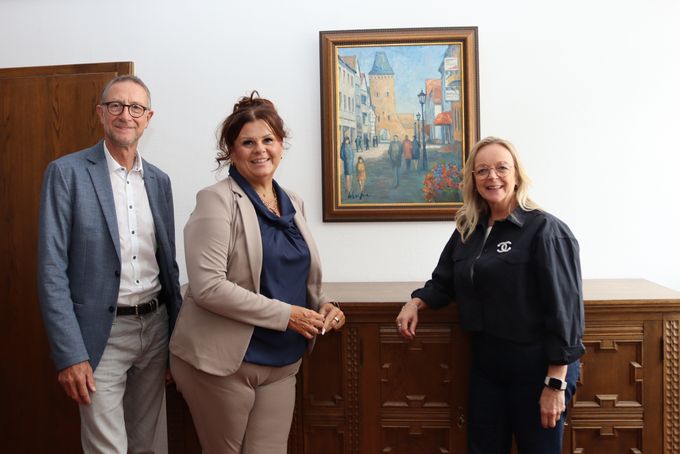 Zwei Mitarbeiter der AOK und Bürgermeisterin Sabine Preiser-Marian stehen neben dem Bild, das an der Wand hängt.
