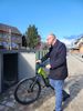 Bürgermeister Sebastian Glatzel steht am Bahnhof vor einer geöffneten Fahrradbox und schiebt ein grünes E-Bike hinein. Die modernen, grau-grünen Boxen befinden sich auf einem gepflasterten Platz neben dem Bahnhofsgebäude.