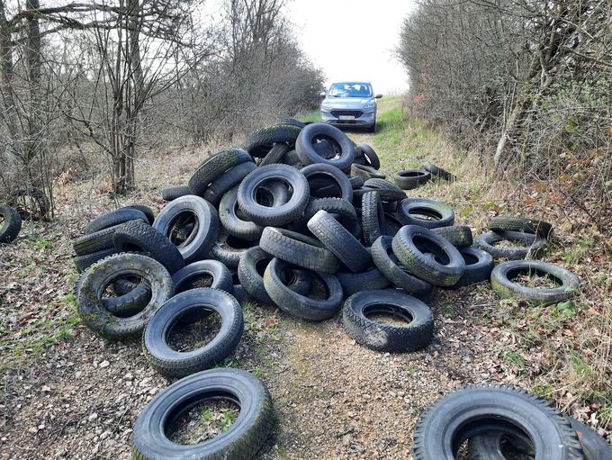 Auf einem Waldweg liegt ein Haufen Altreifen, im Hintergrund steht ein Auto