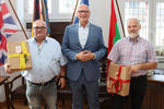 Vor vier Flaggen stehen der Bürgermeister und die Geehrten nebeneinander und schauen in die Kamera.