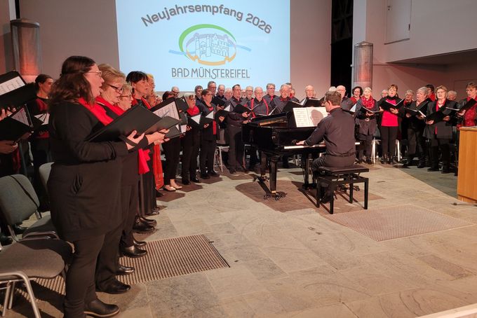 Die Sängerinnen und Sänger des Mutscheider Gesangvereins Eifelklang, die alle in schwarz gekleidet sind, stehen auf der Bühne im Halbrund um ein Klavier.