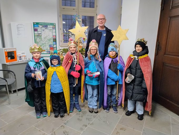 Sechs Sternsinger und Bürgermeister Sebastian Glatzel stehen zum Gruppenfoto aufgereiht vor dem Weihnachtsbaum des Rathauses.