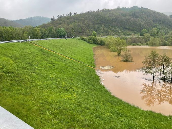 Recht auf dem Bild das braune Wasser im stark gefüllten Hochwasserrückhaltebecken Eicherscheid, links der grüne Damm mit Treppe