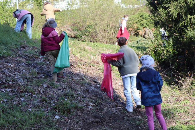 Kinder suchen mit einer grünen und einer roten Mülltüte in den Beeten im Kurgarten nach Müll.