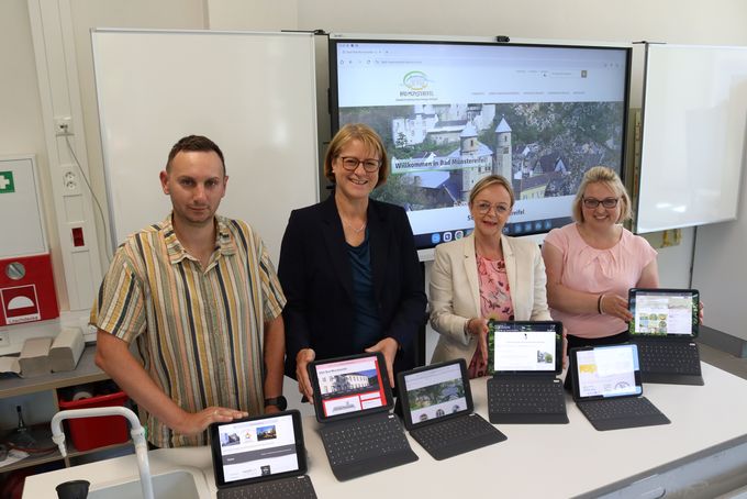 Alexander Smith, Andrea Cosman, Sabine Preiser-Marian und Stephanie Schmitz stehen vor einer digitalen Tafel mit Bildschirm. Vor ihnen Tablets auf einem Tisch.