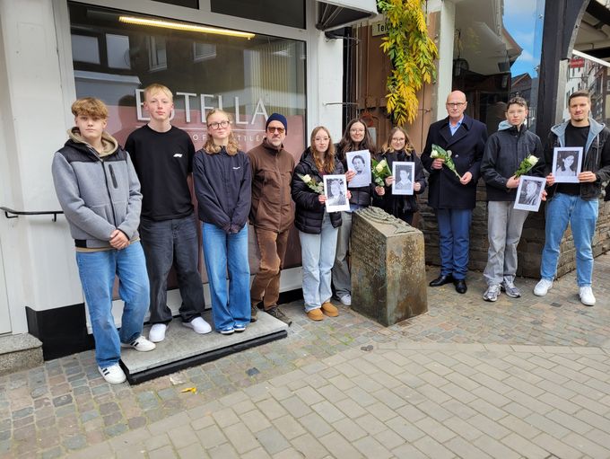 Bürgermeister Sebastian Glatzel und neun weitere Personen stehen mit Blumen und Fotos der Deportierten an der Gedenkstele.