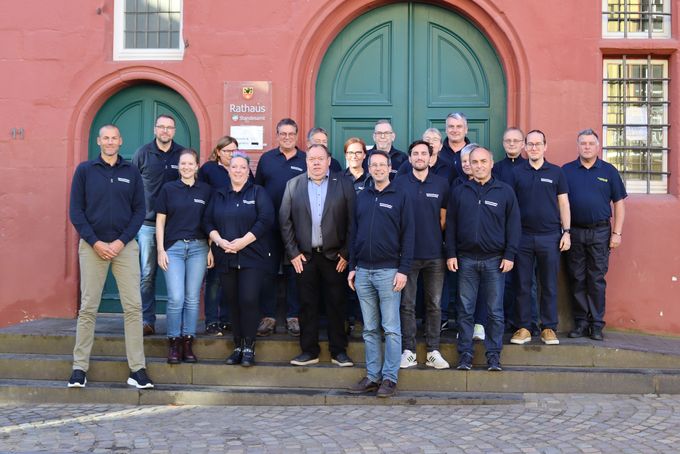 Die Delegation aus dem Bezirksamt Bergedorf, die alle einheitliche blaue T-Shirts tragen, stehen mit den Dozenten zum Gruppenbild vor dem roten Rathaus in Bad Münstereifel.