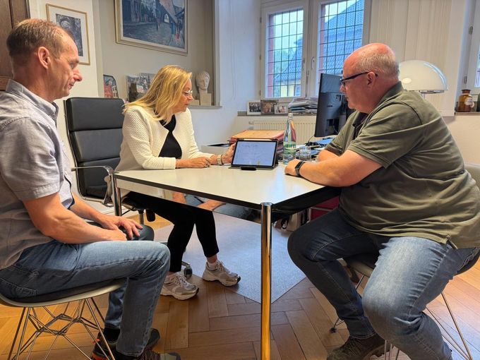 Zwei Mitarbeiter der Stadtwerke sitzen mit Bürgermeisterin Sabine Preiser-Marian an deren Schreibtisch und schauen auf ein Tablet.
