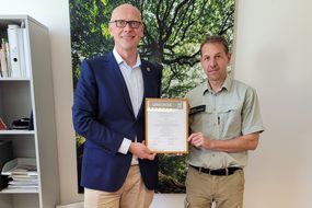 Sebastian Glatzel und Stefan Lott halten das PEFC-Zertifikat in die Kamera.