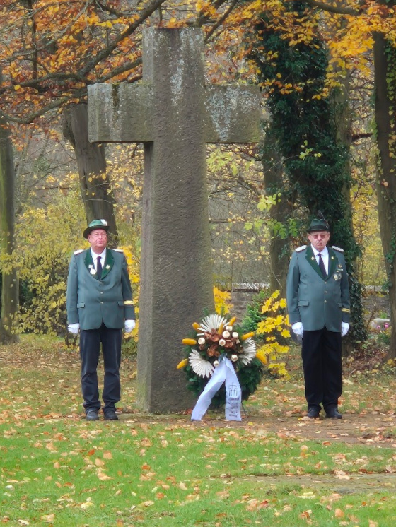 Je ein Mitglied der St. Sebastianus Schützenbruderschaft steht rechts und links neben dem Ehrenkreuz auf dem Friedhof. 