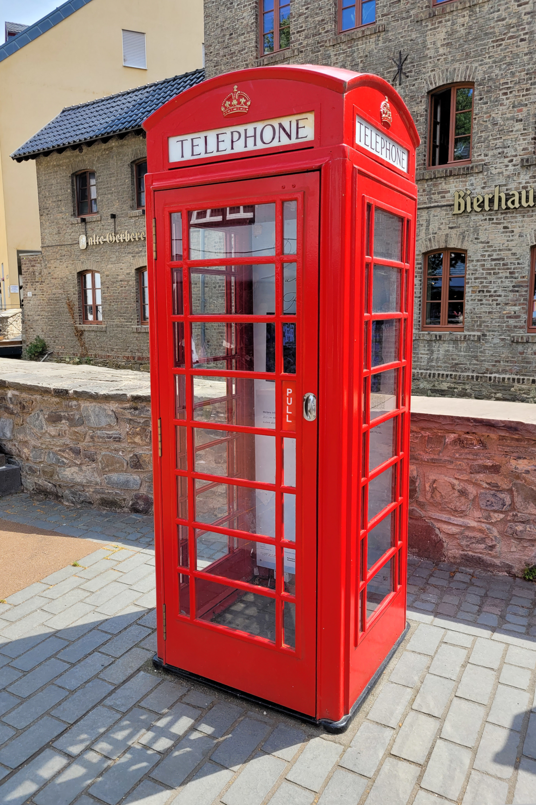 Eine rote, englische Telefonzelle vor einem Haus aus Bruchstein.